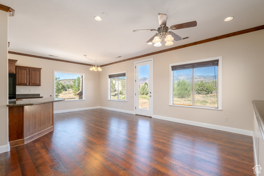 Unfurnished living room featuring recessed lighting, dark wood-style floors, ornamental molding, a ceiling fan, and a chandelier