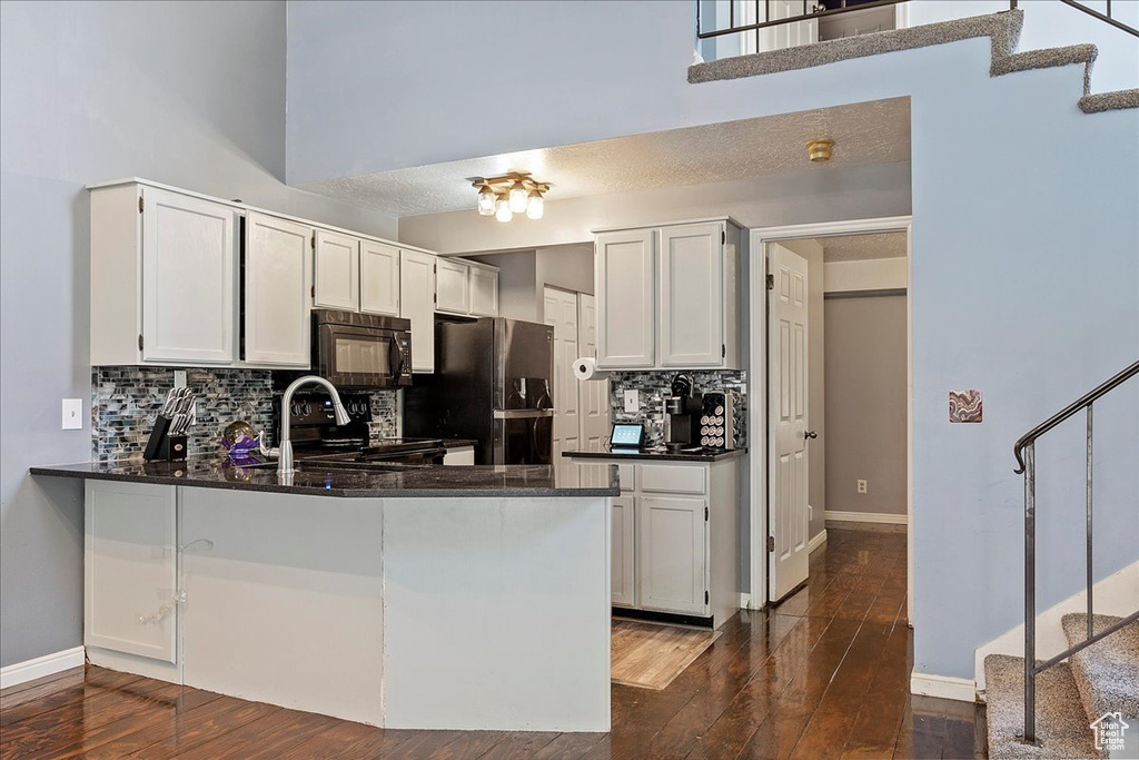 Kitchen with black appliances, a peninsula, decorative backsplash, and dark wood-type flooring