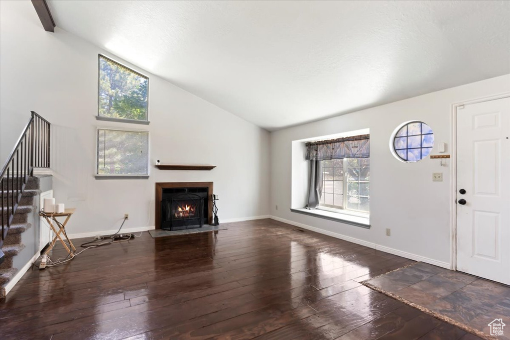 Unfurnished living room featuring stairway, a fireplace with flush hearth, hardwood / wood-style flooring, and high vaulted ceiling