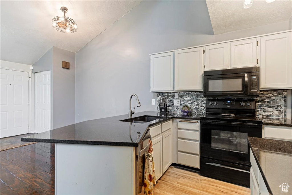 Kitchen featuring black appliances, lofted ceiling, a peninsula, light wood-type flooring, and tasteful backsplash