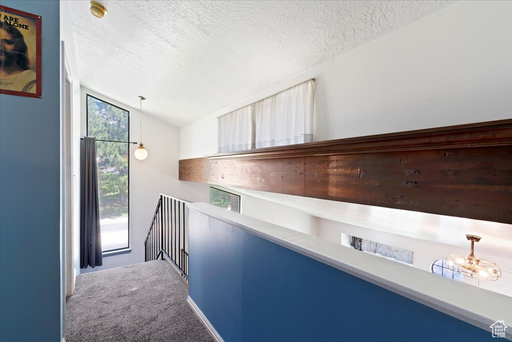 Corridor with a textured ceiling, an upstairs landing, carpet floors, and lofted ceiling