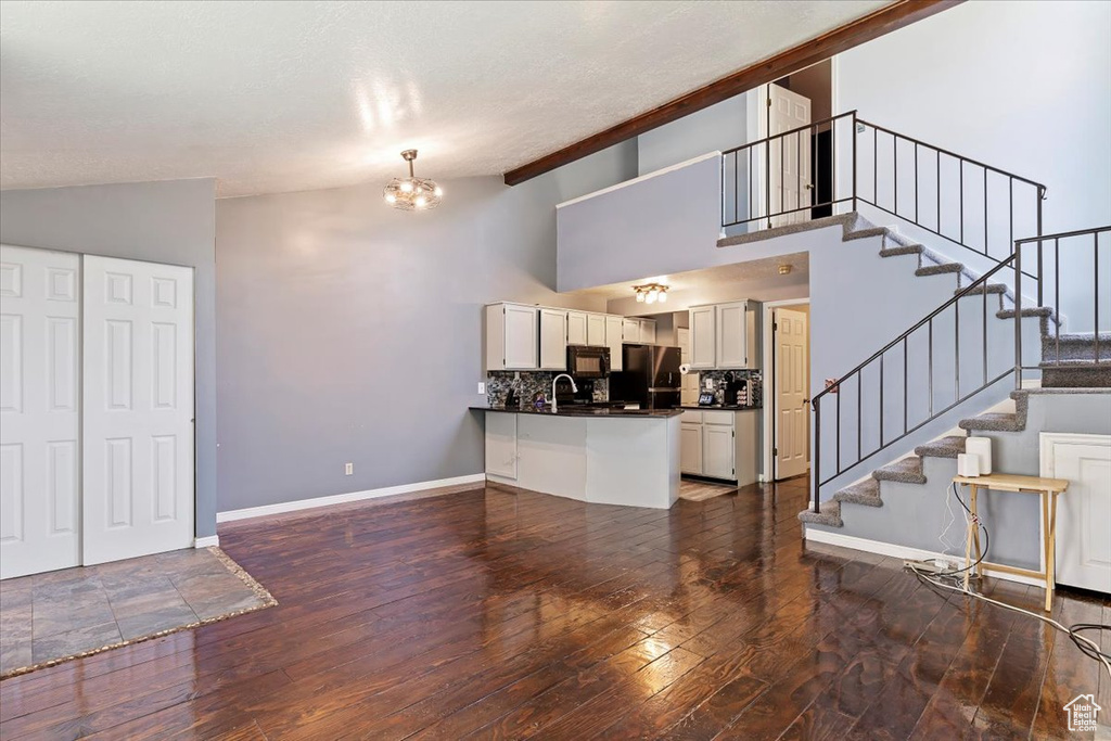 Unfurnished living room featuring hardwood / wood-style floors, stairway, a chandelier, and high vaulted ceiling