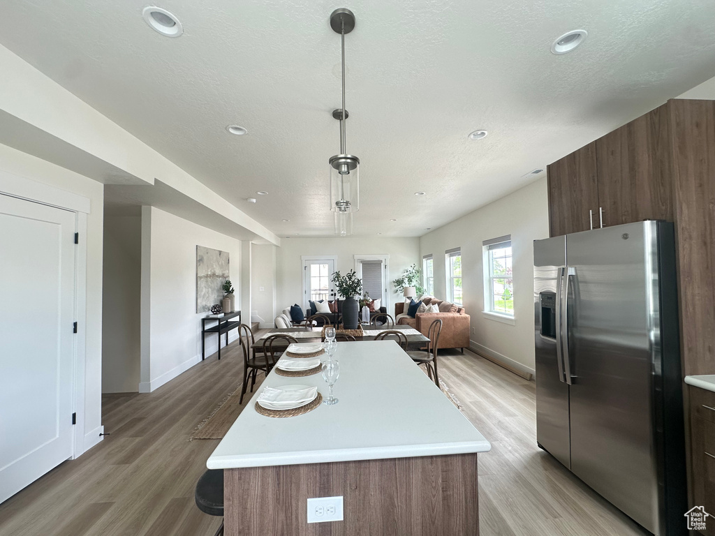 Kitchen featuring stainless steel fridge with ice dispenser, light countertops, open floor plan, light wood-style floors, and recessed lighting