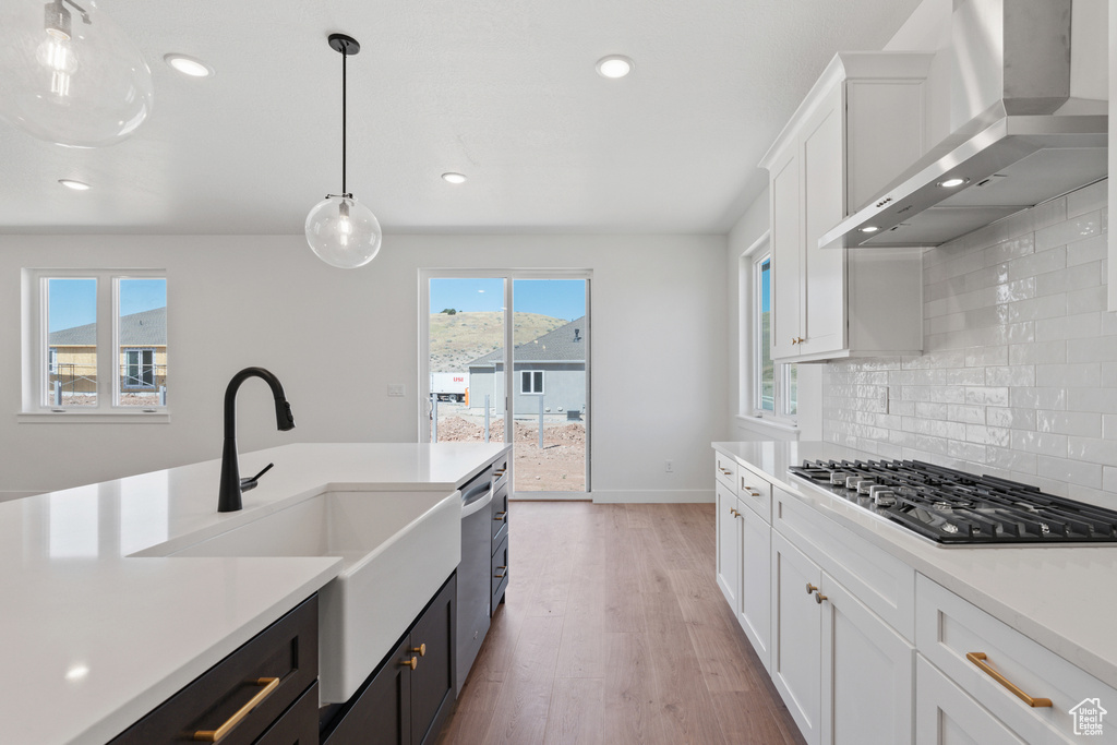 Kitchen with wall chimney range hood, stainless steel appliances, light countertops, backsplash, and recessed lighting