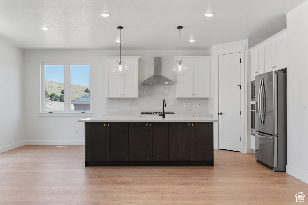 Kitchen with wall chimney exhaust hood, stainless steel fridge with ice dispenser, light countertops, white cabinets, and light wood-style floors