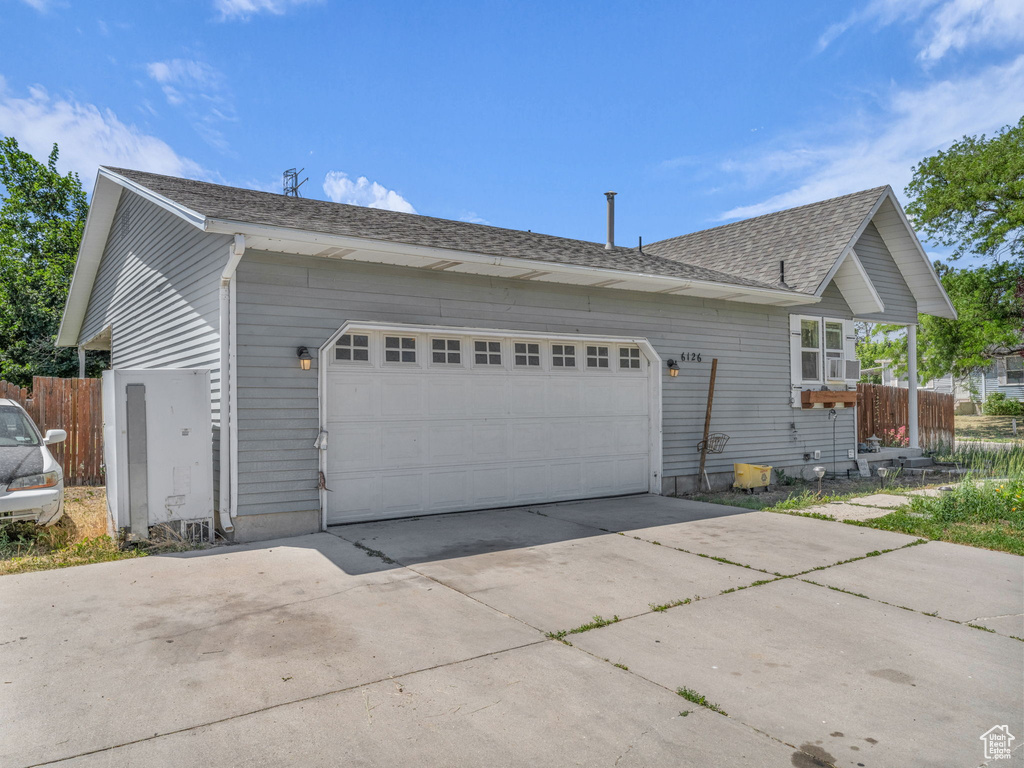 View of side of property featuring driveway, a garage, and roof with shingles