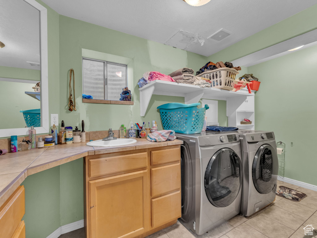 Laundry area featuring washer and dryer, light tile patterned floors, and cabinet space