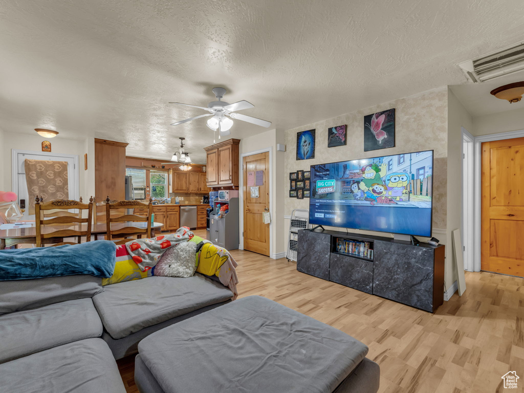 Living room with light wood-type flooring, a ceiling fan, and a textured ceiling
