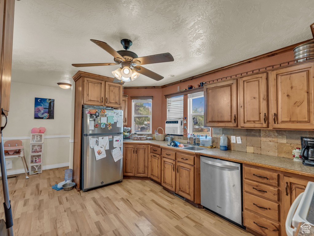 Kitchen with appliances with stainless steel finishes, light wood-style floors, a ceiling fan, brown cabinets, and a textured ceiling