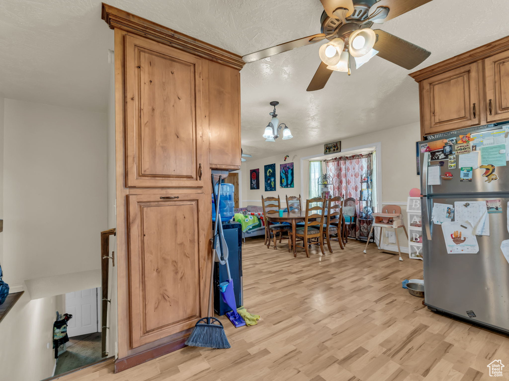 Kitchen featuring freestanding refrigerator, a ceiling fan, light wood finished floors, and brown cabinetry