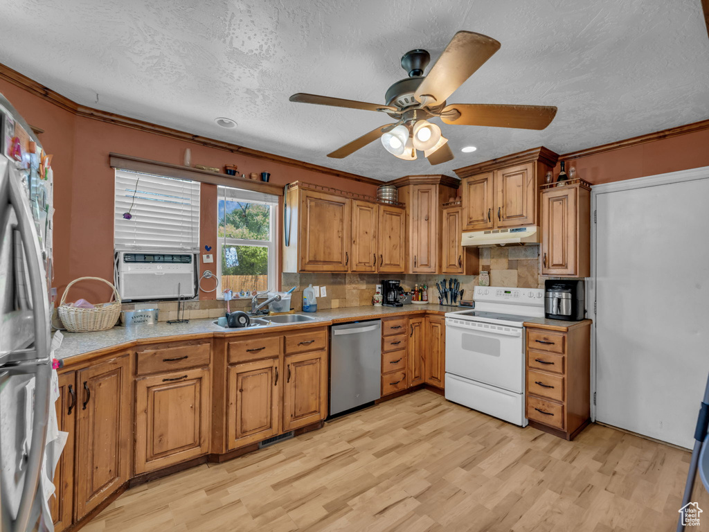 Kitchen with stainless steel appliances, under cabinet range hood, light wood-style floors, brown cabinets, and a textured ceiling
