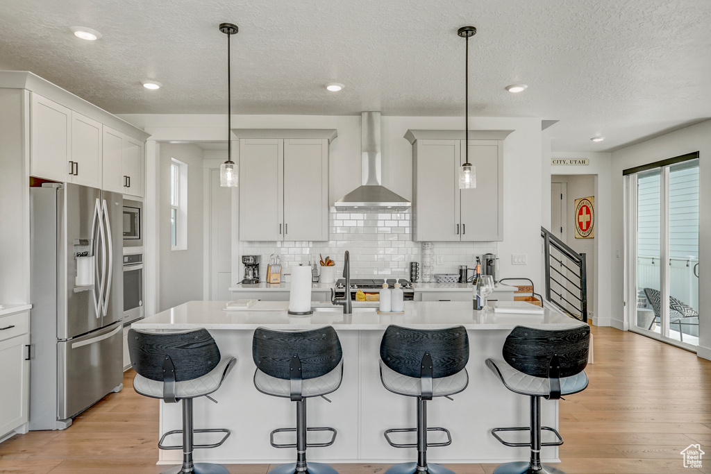Kitchen with stainless steel appliances, wall chimney exhaust hood, a breakfast bar area, light wood finished floors, and a textured ceiling