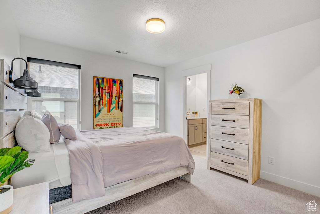 Bedroom featuring a textured ceiling, ensuite bathroom, and light colored carpet