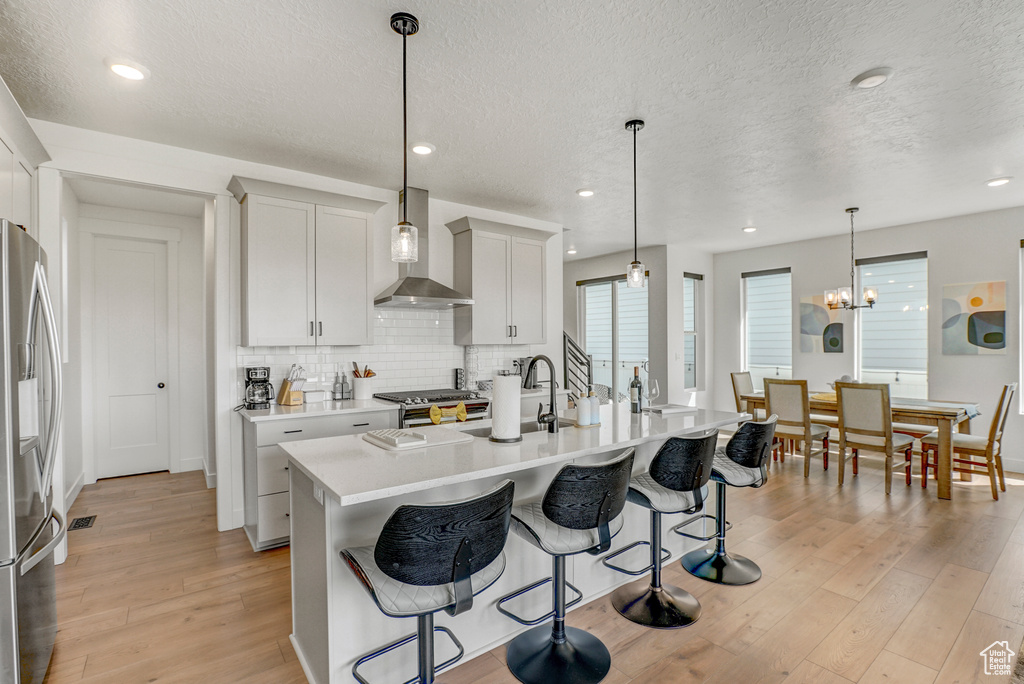 Kitchen featuring appliances with stainless steel finishes, wall chimney range hood, light wood-style floors, a kitchen bar, and backsplash