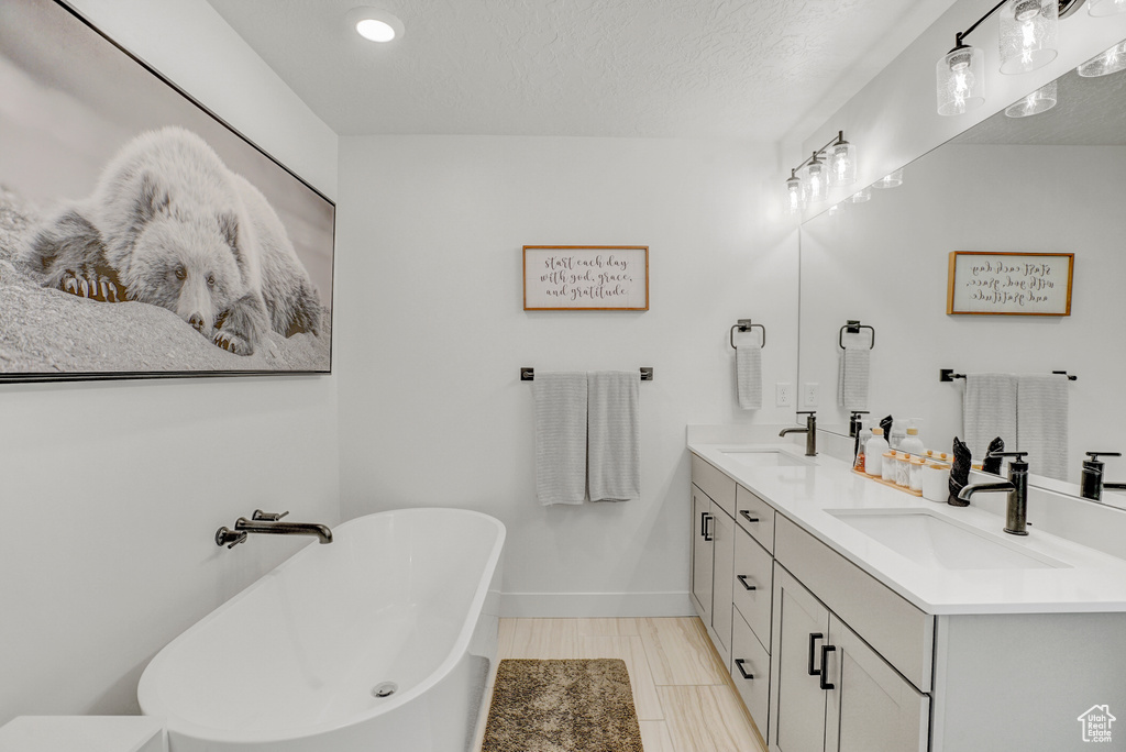 Bathroom featuring double vanity, a freestanding tub, recessed lighting, and a textured ceiling