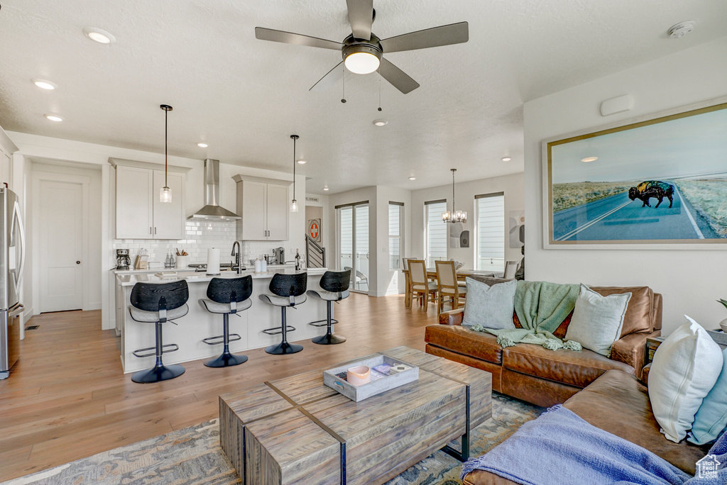 Living room featuring light wood-style flooring, a ceiling fan, recessed lighting, and a chandelier
