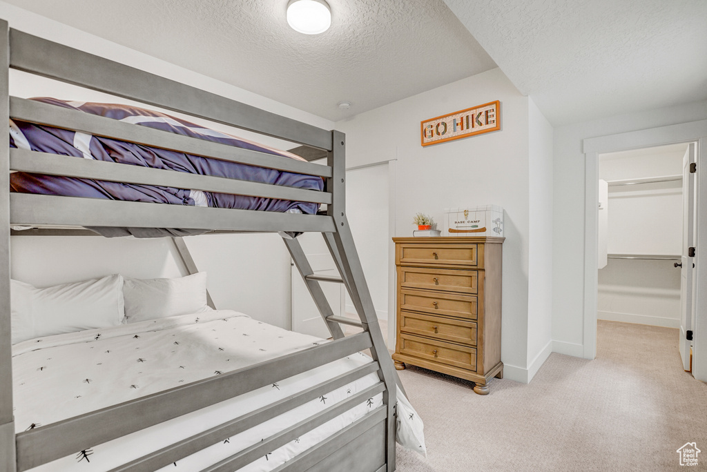 Bedroom featuring a textured ceiling, light carpet, and a walk in closet