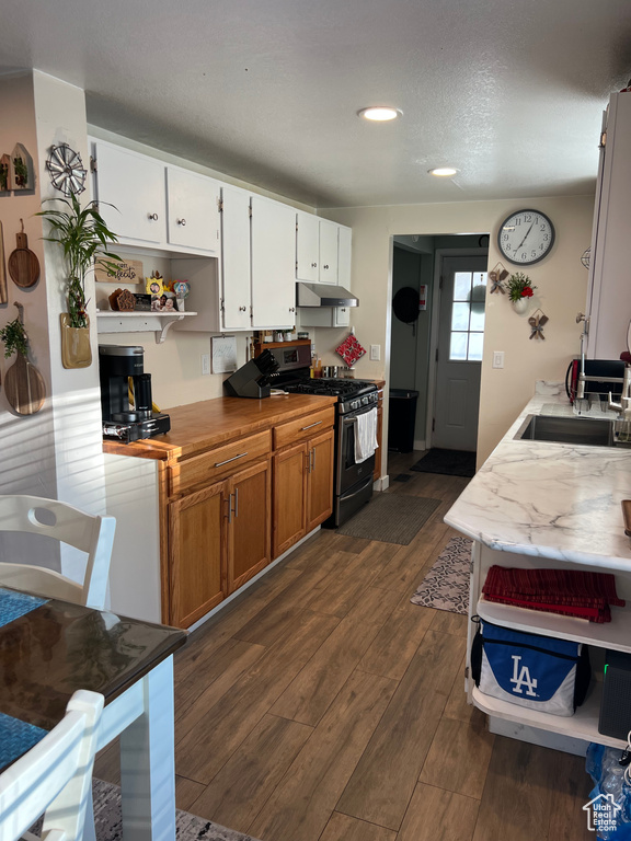 Kitchen featuring stainless steel range with gas cooktop, open shelves, under cabinet range hood, dark wood-type flooring, and brown cabinetry