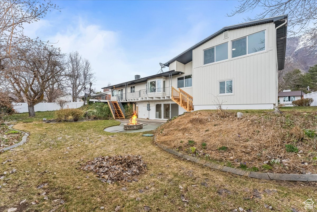 Back of property featuring an outdoor fire pit, stairs, a deck, and a lawn