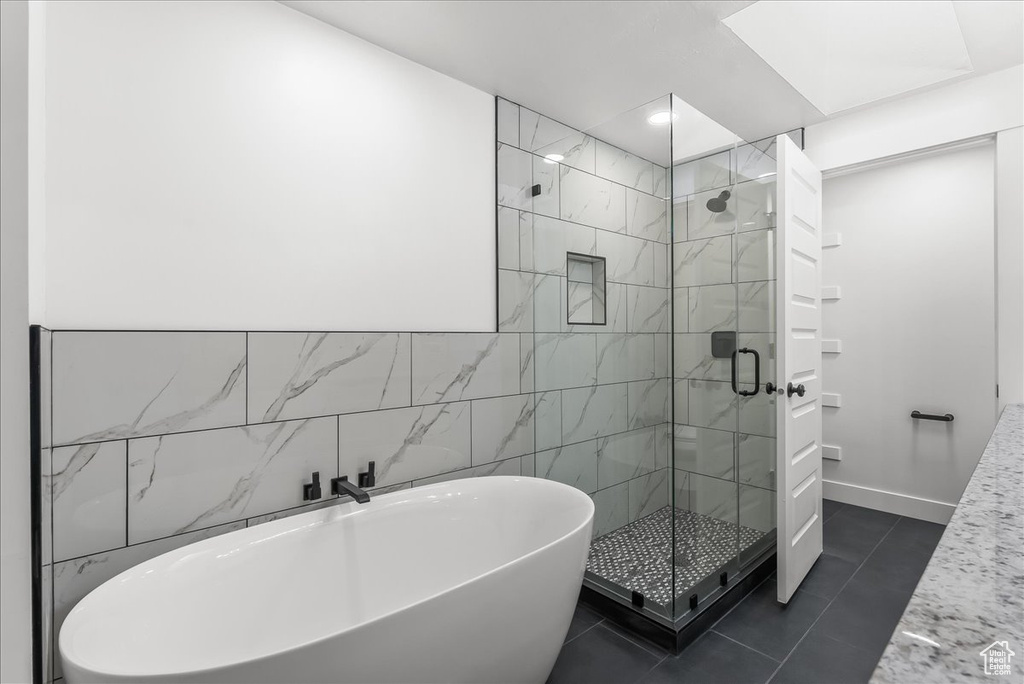 Full bath featuring a freestanding bath, a stall shower, tile patterned flooring, and tile walls