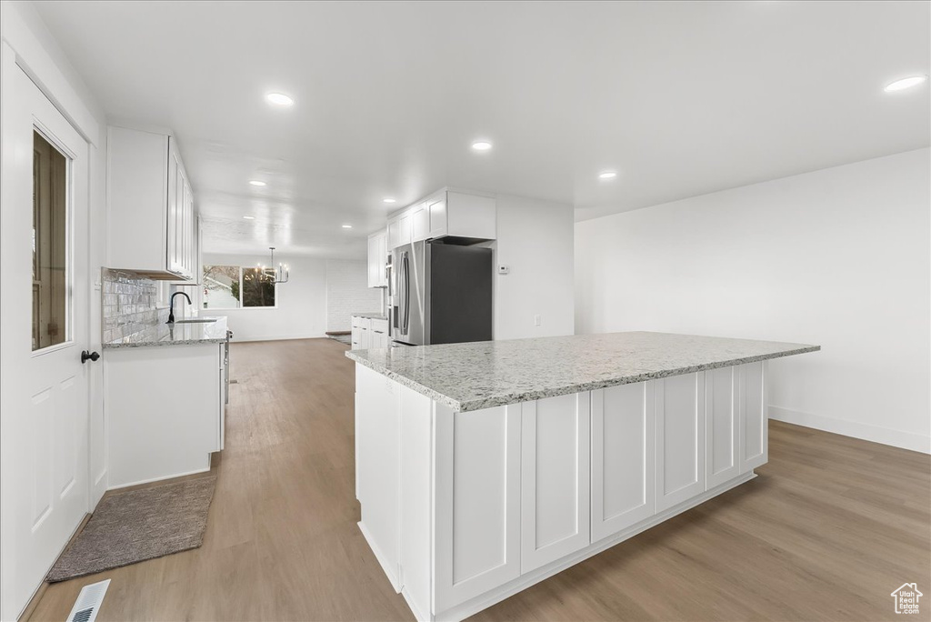 Kitchen featuring stainless steel fridge with ice dispenser, white cabinetry, light wood-type flooring, recessed lighting, and light stone counters