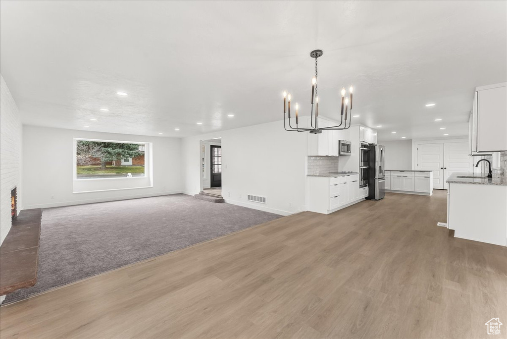 Unfurnished living room featuring recessed lighting, a chandelier, light wood finished floors, and a brick fireplace