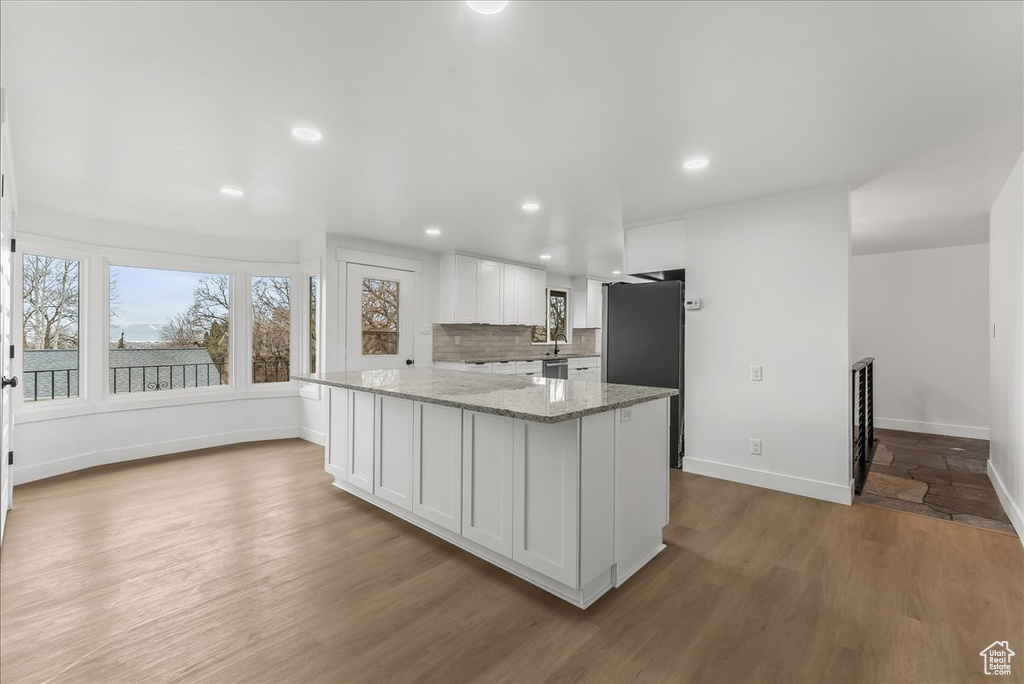 Kitchen with white cabinetry, wood finished floors, light stone counters, freestanding refrigerator, and decorative backsplash