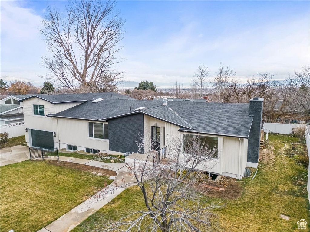 Rear view of property featuring a garage, a shingled roof, a chimney, and concrete driveway