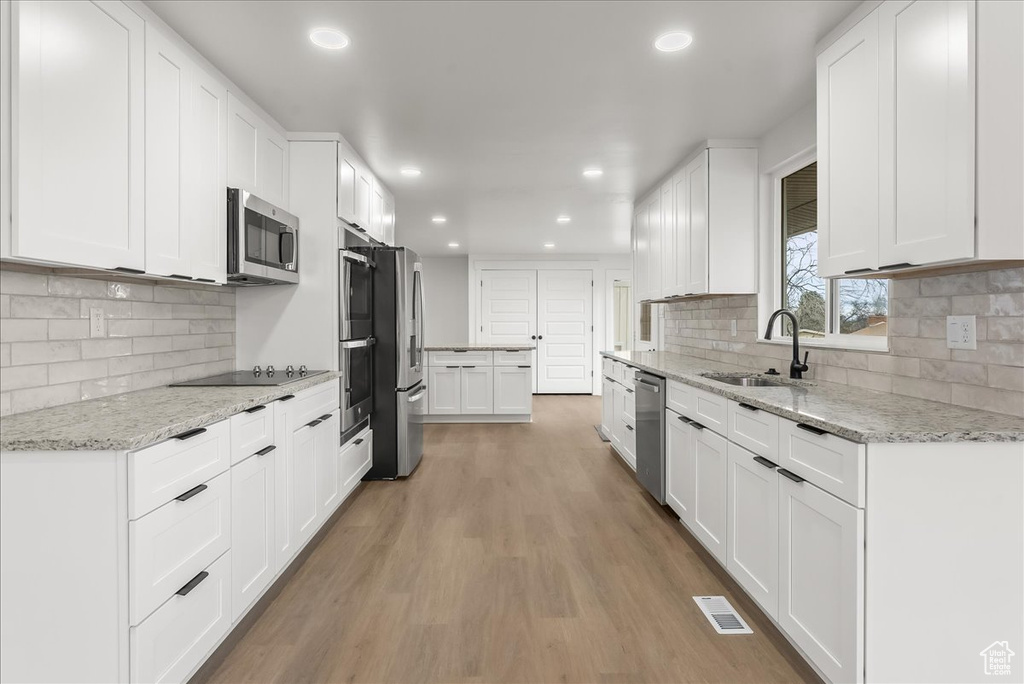 Kitchen with appliances with stainless steel finishes, recessed lighting, light wood finished floors, decorative backsplash, and white cabinetry