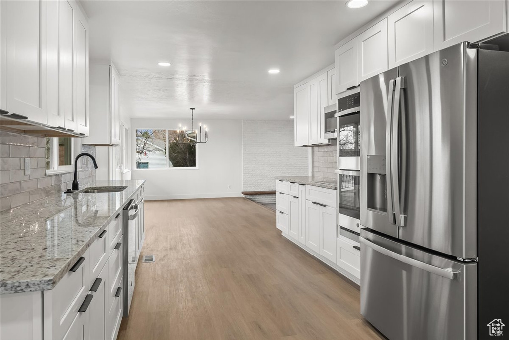 Kitchen featuring appliances with stainless steel finishes, backsplash, white cabinetry, a chandelier, and light wood finished floors