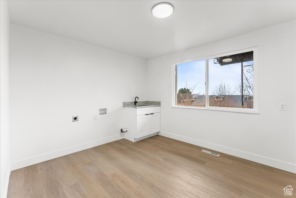 Washroom featuring electric dryer hookup, hookup for a washing machine, light wood-style floors, and cabinet space