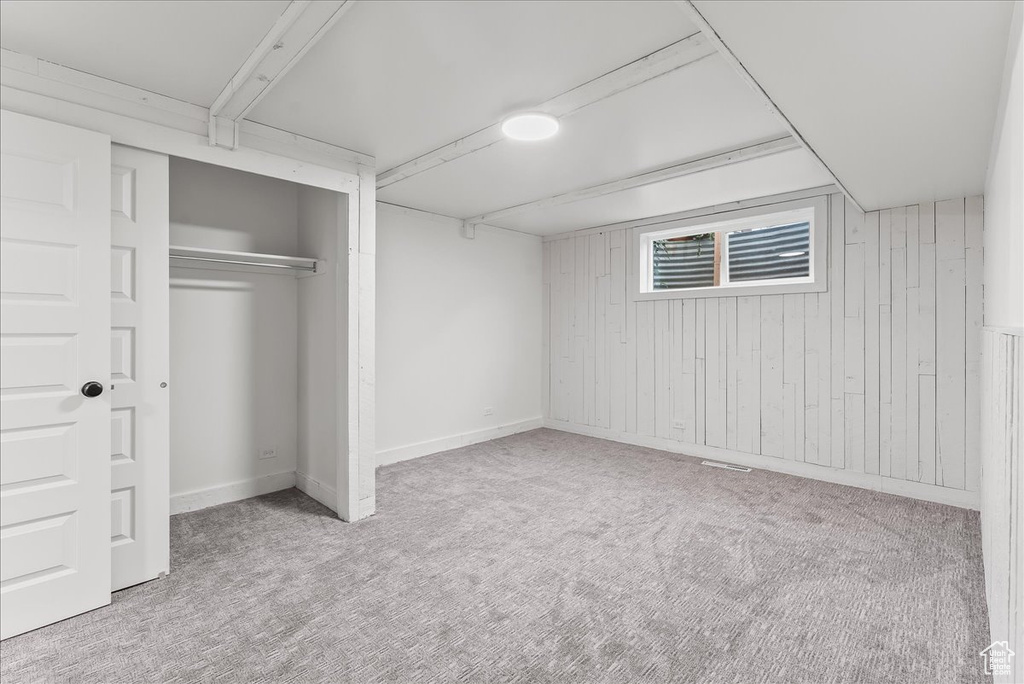 Unfurnished bedroom featuring carpet flooring, wood walls, and a closet