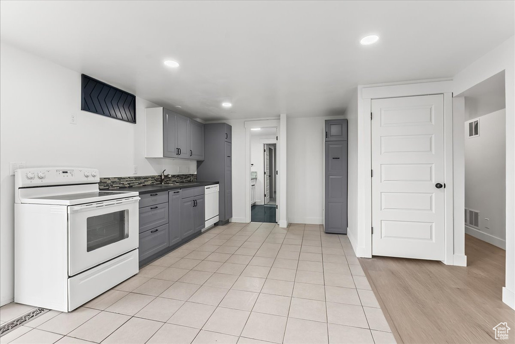 Kitchen featuring white appliances, gray cabinetry, recessed lighting, dark countertops, and light wood-type flooring