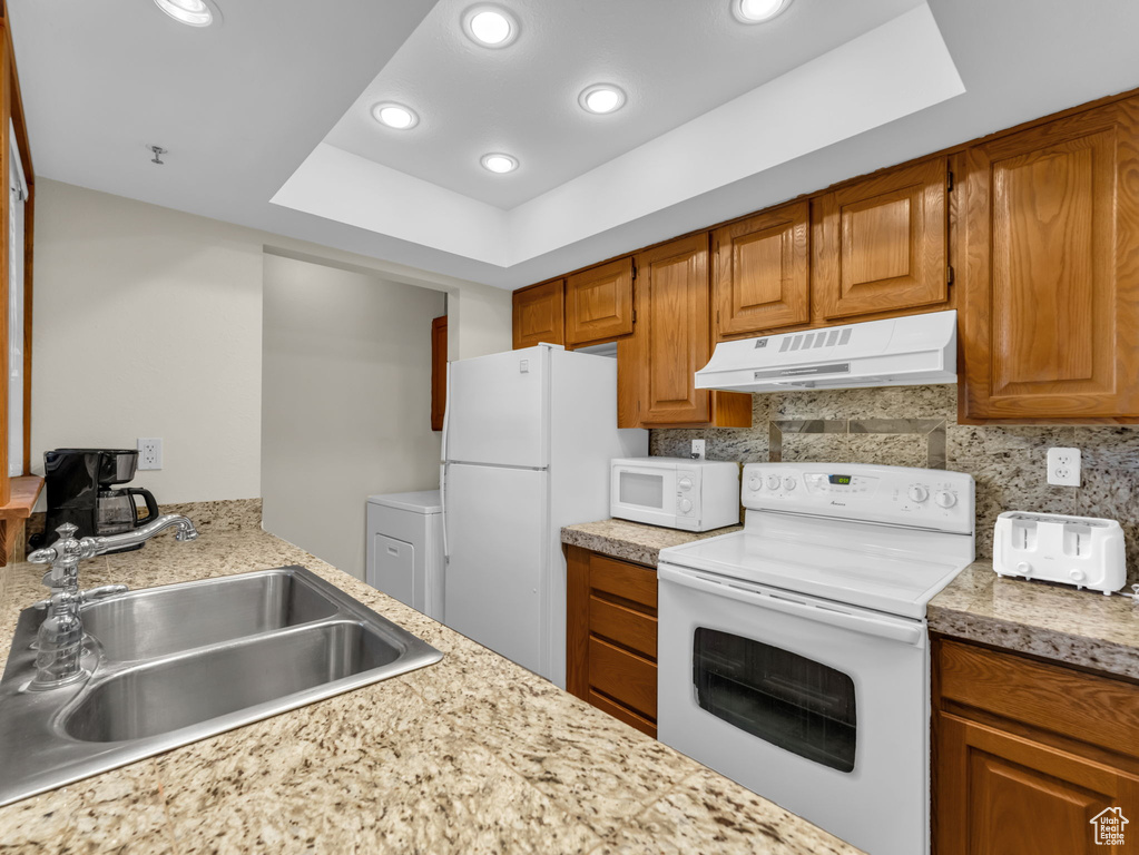 Kitchen featuring white appliances, under cabinet range hood, washer / clothes dryer, light countertops, and a raised ceiling