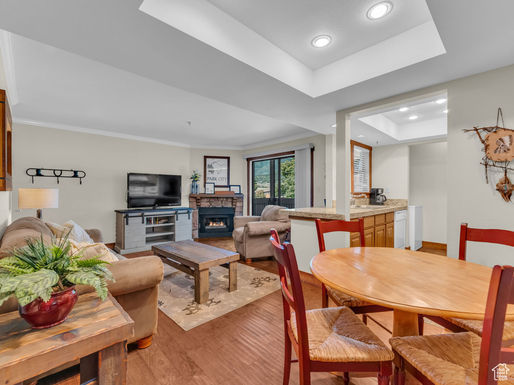 Dining room featuring light wood finished floors, a fireplace, a tray ceiling, recessed lighting, and ornamental molding