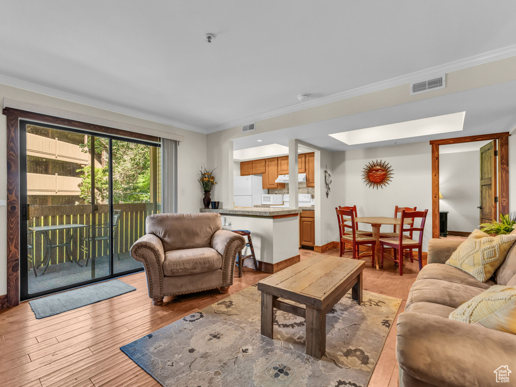 Living room with ornamental molding, light wood-type flooring, and a skylight