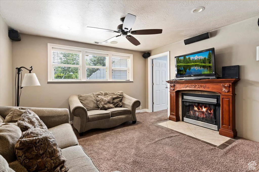Living room with light colored carpet, a ceiling fan, a tile fireplace, and a textured ceiling