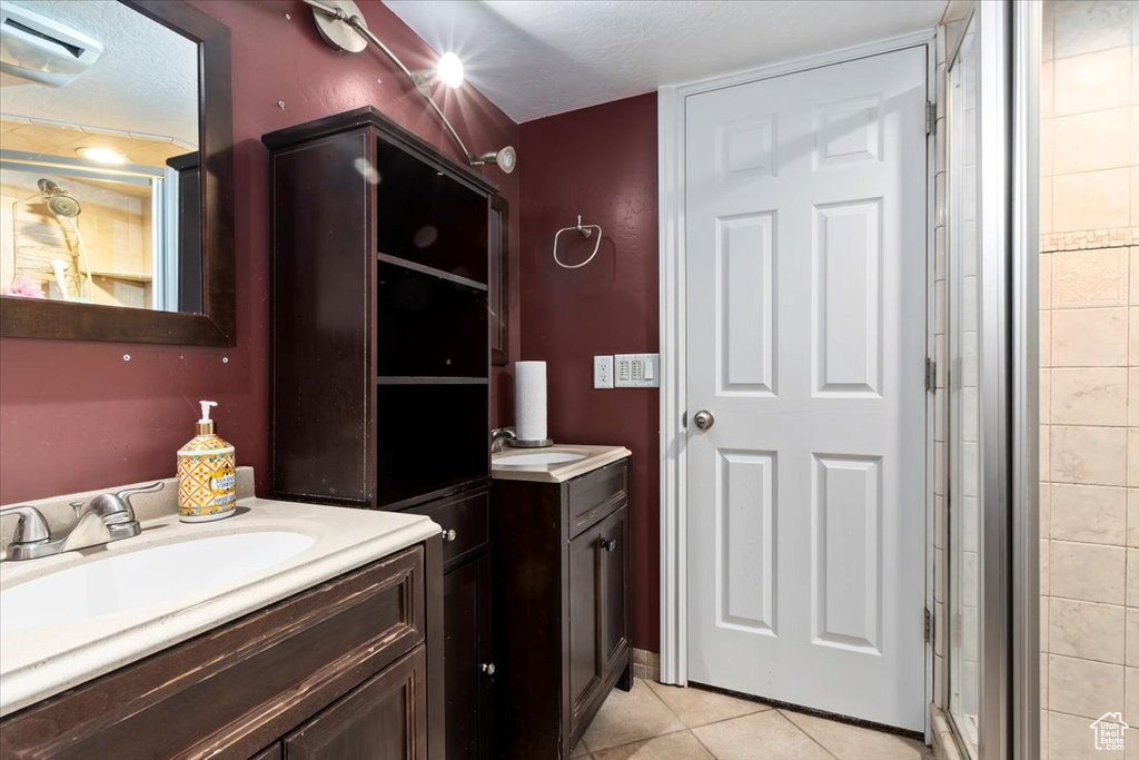 Full bath featuring two vanities, tile patterned flooring, an AC wall unit, a shower stall, and a textured ceiling