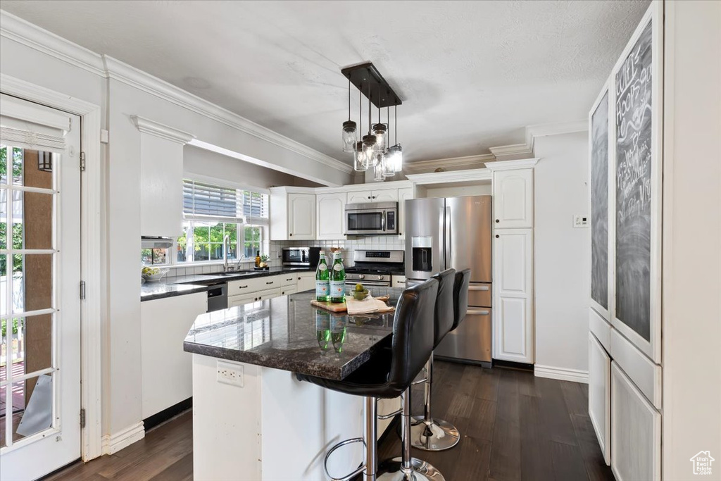 Kitchen with stainless steel appliances, white cabinets, dark wood-type flooring, decorative backsplash, and ornamental molding