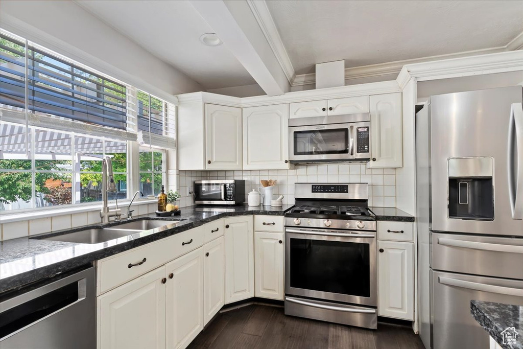 Kitchen with stainless steel appliances, dark wood-type flooring, backsplash, dark stone countertops, and ornamental molding