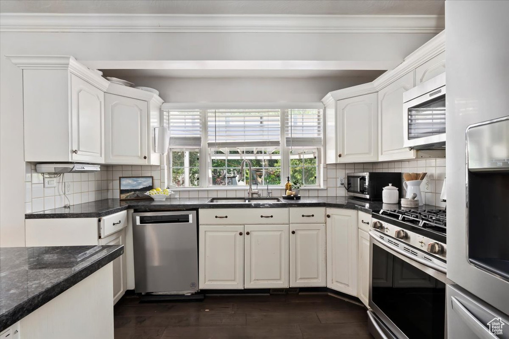 Kitchen with appliances with stainless steel finishes, white cabinetry, backsplash, and ornamental molding