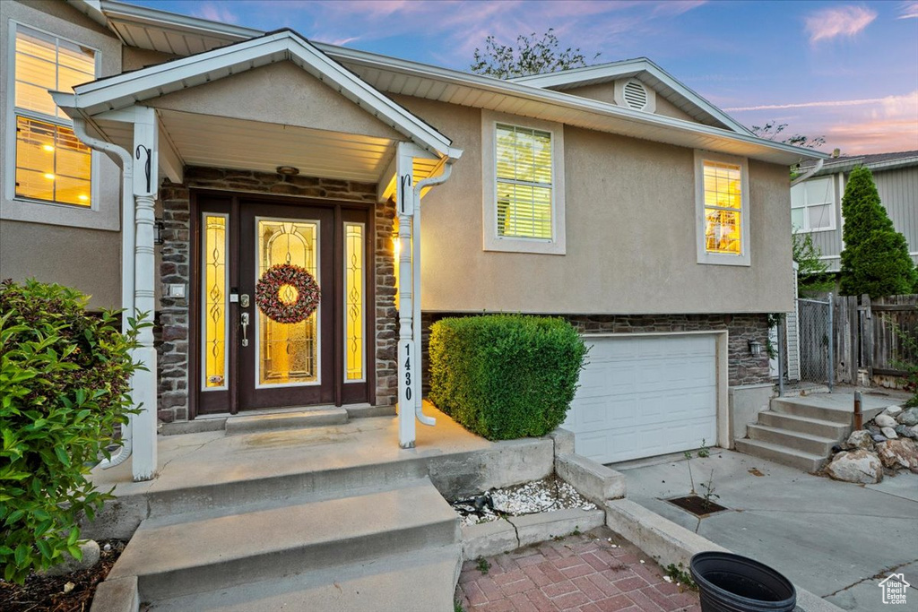 Exterior entry at dusk with stone siding, stucco siding, a garage, and driveway