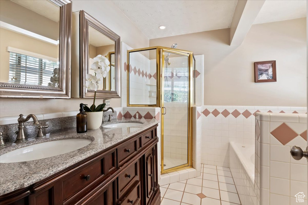 Bathroom featuring tile walls, tile patterned flooring, a shower stall, a bath, and double vanity