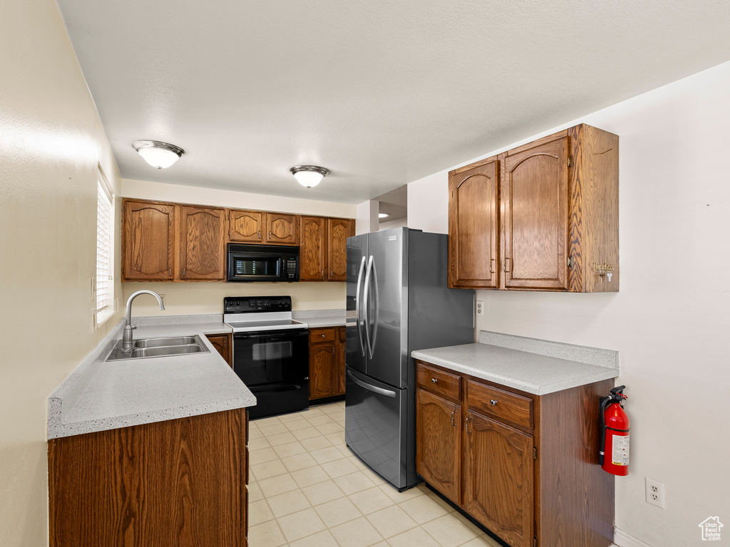 Kitchen featuring black microwave, range with electric cooktop, stainless steel fridge, light countertops, and light tile patterned flooring