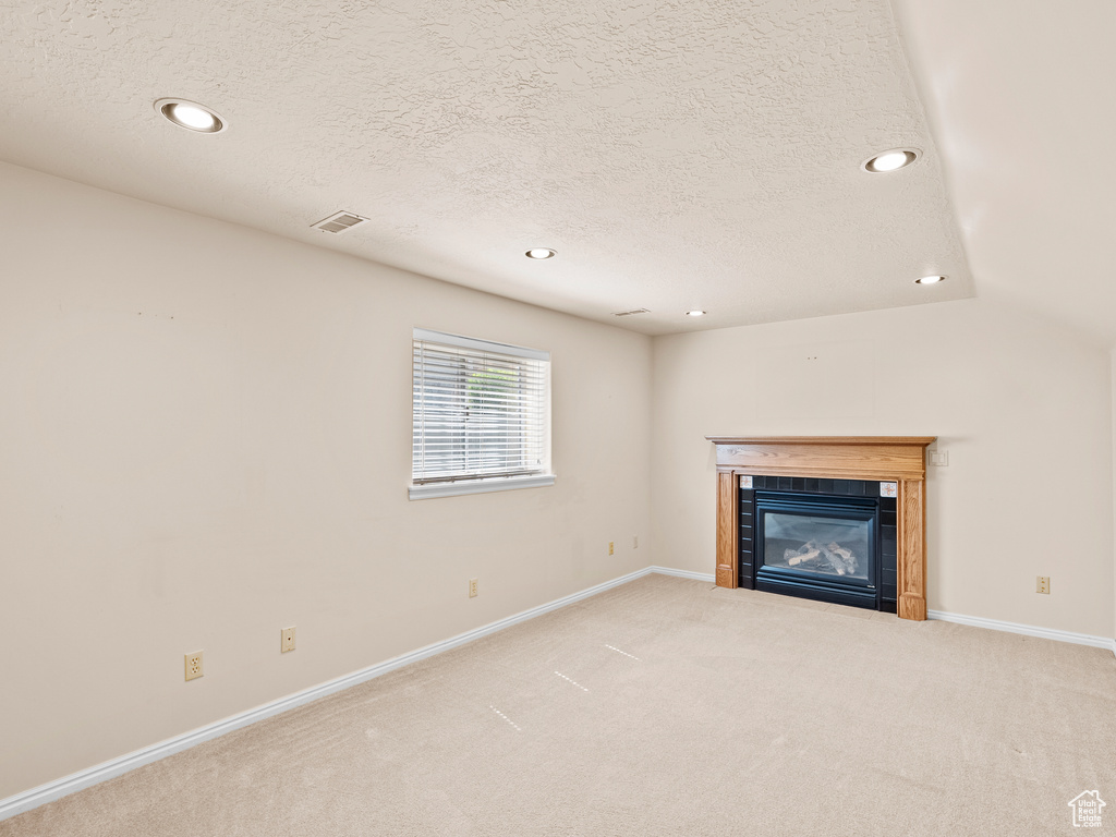 Unfurnished living room featuring recessed lighting, a tiled fireplace, a textured ceiling, and carpet flooring