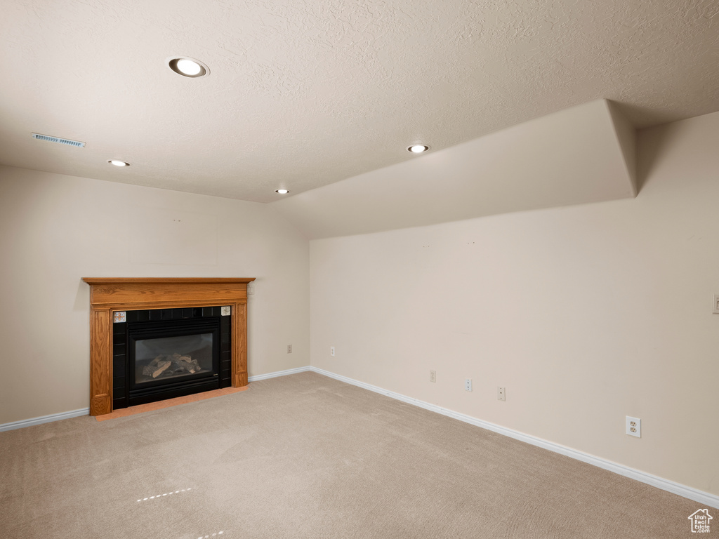 Unfurnished living room with carpet, a fireplace with flush hearth, recessed lighting, lofted ceiling, and a textured ceiling