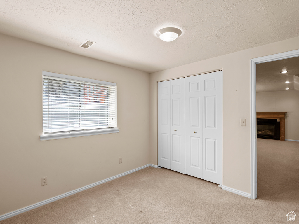 Unfurnished bedroom featuring light carpet, a closet, a fireplace, and a textured ceiling