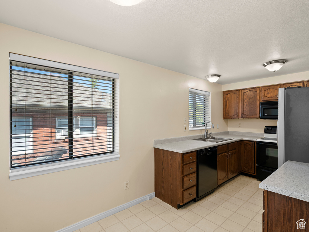 Kitchen featuring black appliances, light countertops, light tile patterned floors, and brown cabinetry