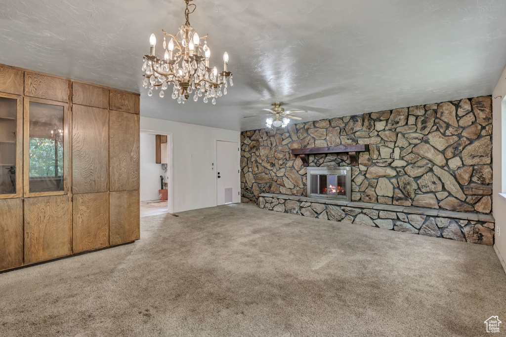 Unfurnished living room with ceiling fan, carpet floors, a chandelier, and a fireplace