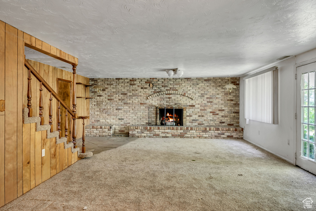 Unfurnished living room featuring carpet flooring, a brick fireplace, brick wall, stairs, and a textured ceiling